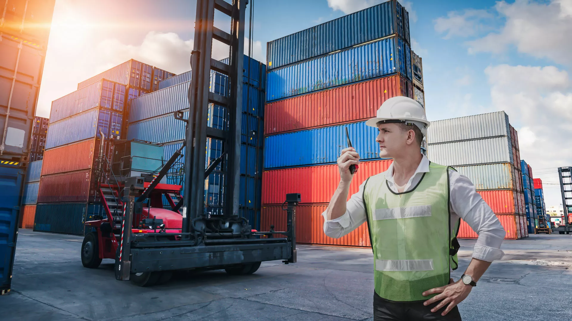 Logistiker mit Walkie Talkie in der Hand steht im Frachthafen vor Frachtcontainern